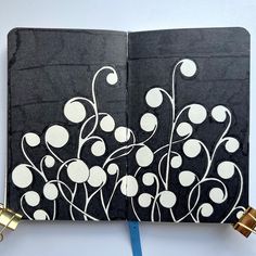 an open notebook with black paper and white designs on the pages, next to a gold lock