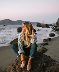 a woman sitting on top of a rock near the ocean