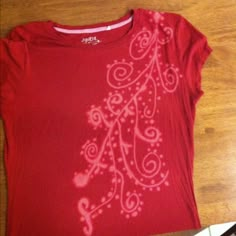 a red t - shirt with white swirls on it sitting on top of a wooden floor