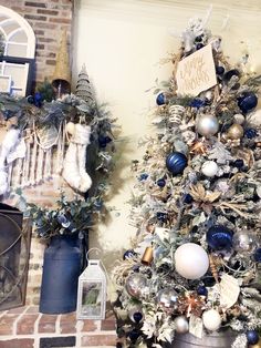 a decorated christmas tree in front of a fireplace with blue and silver ornaments on it