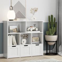 a white bookcase with three drawers and two plants on top, next to a potted cactus