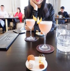 a woman sitting at a table with two drinks in front of her