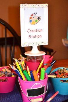 there is a pink bucket full of crayons and pencils on the table