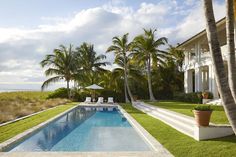 a pool in front of a house with palm trees on the lawn and an umbrella over it