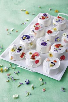 there are many small cakes with flowers on the tray and petals scattered all over the table