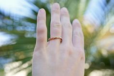 a woman's hand with a gold ring on top of her finger and palm tree in the background