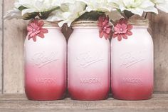 three pink mason jars with white and red flowers in them