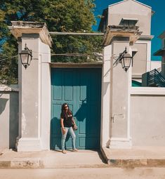 a woman standing in front of a blue door with two pillars and a light pole