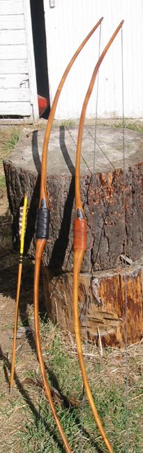 two wooden bow and arrows in front of a tree stump with a shed in the background