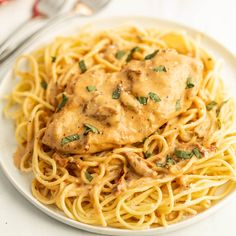 a white plate topped with pasta covered in gravy next to a fork and knife