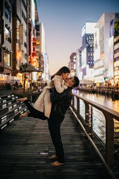 a man and woman are kissing on a pier in the middle of a city at night