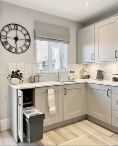 a white kitchen with grey cabinets and a large clock on the wall above the sink