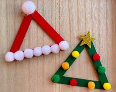 two christmas trees made out of popsicle sticks and pom - poms on a wooden surface