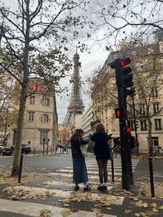 two women are standing on the street corner in front of the eiffel tower