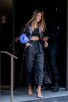 a woman in black pants and jacket walking out of a building with her hand on her hip