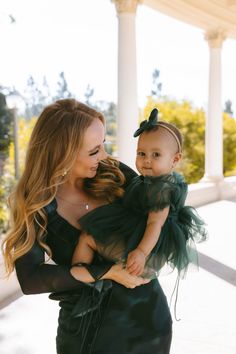 a woman holding a baby in her arms and smiling at the camera while wearing a green dress