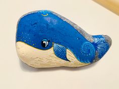 a painted rock with a blue whale on it's side, sitting on a white surface