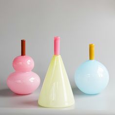 three different colored vases sitting next to each other on a white counter top in front of a gray wall