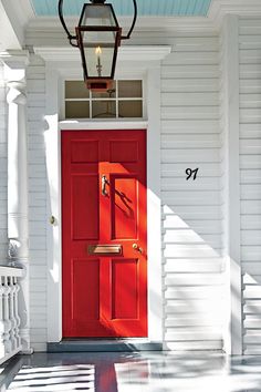 a bright red door sits in front of a white house with black shutters on either side