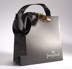 a silver shopping bag with a black ribbon around the handle and gold hardware on top