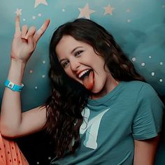 a young woman making the peace sign with her fingers while sitting in front of a wall