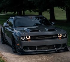 the front end of a gray sports car parked on a dirt road near some trees