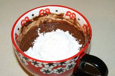 a red and white coffee mug filled with chocolate pudding, powdered sugar and cinnamon