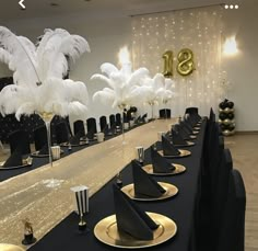 a long table with black and gold place settings, white feather centerpieces on each plate