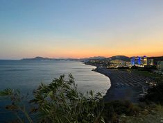 the sun is setting over an ocean with buildings in the distance and mountains in the background