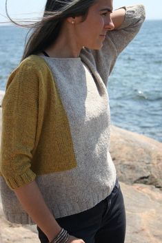 a woman standing by the ocean with her hair in the wind and wearing a sweater