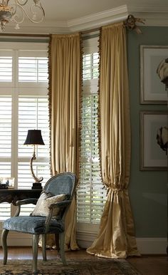 a living room filled with furniture and windows covered in draping next to a chandelier