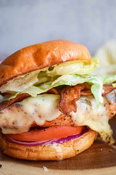 a grilled chicken sandwich with lettuce, tomato and bacon on a wooden cutting board