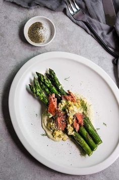 a white plate topped with asparagus next to a bowl of seasoning and a fork