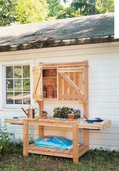 a potting bench with plants on it in front of a white house and window