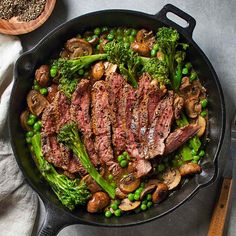 a skillet filled with steak, mushrooms and broccoli on top of a table