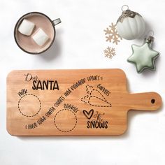 a wooden cutting board with santa written on it next to christmas ornaments and other decorations