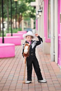 a young boy dressed in black and white holding a baseball bat on a sidewalk with pink benches behind him