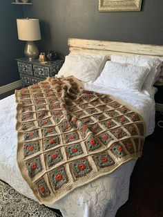 a bed with a blanket on top of it next to a night stand and lamp