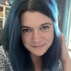 a woman with blue hair is posing for a photo in front of a bookshelf