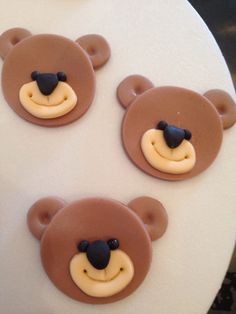 three chocolate teddy bears on top of a white cake with cream frosting in the shape of faces