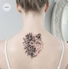 a woman's back neck with a wolf and flowers tattoo on her left shoulder