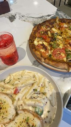 two pizzas and some pasta on a table with drinks next to it, one is topped with cheese