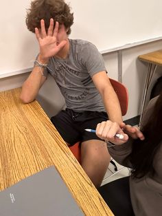 a young man sitting at a table with his hand up to his face while another person sits in front of him