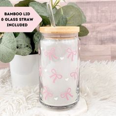 a glass jar with pink bows on it and a bamboo lid next to a potted plant