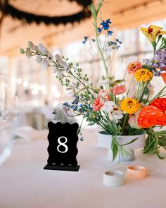 an arrangement of flowers and candles on a table with the number eight in front of it