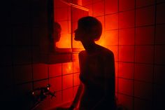 a woman standing in front of a bathroom mirror with red light shining on her face