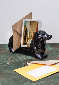 a black dachshund figurine sitting next to an envelope on a table