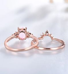 two wedding rings with pink opal in the middle on a white table next to flowers