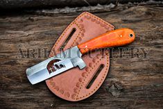 an orange handled knife sitting on top of a piece of leather with stitched edges