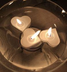 three lit candles in a glass bowl with hearts on the bottom and one candle inside